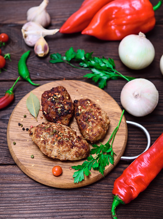 Three meat cutlets with spices on a wooden kitchen board with fresh vegetables, top viewの写真素材
