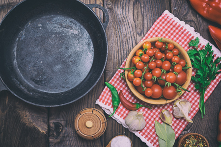Empty black cast-iron frying pan and red cherry tomatoes in a wooden plateの写真素材
