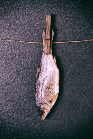 dried salted fish suspended from the tail on a rope with a wooden clothespinの写真素材