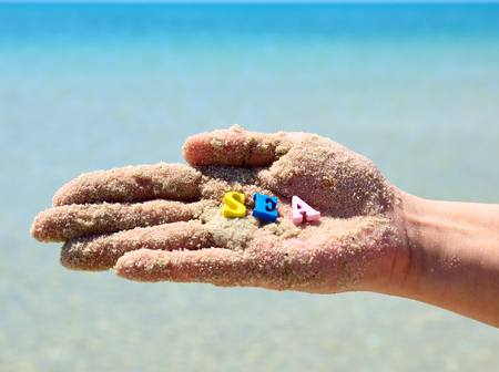 human hand in the sand, on the palm of the word sea of multicolored wooden letters