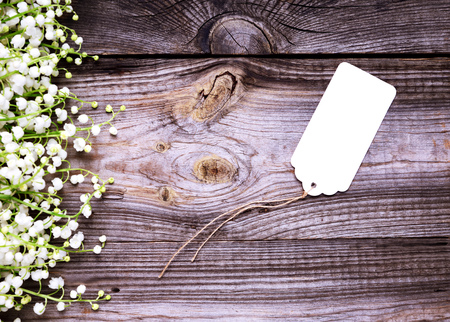 empty white paper tag with a rope on a gray wooden background, on the side a bouquet of blossoming lilies of the valleyの写真素材