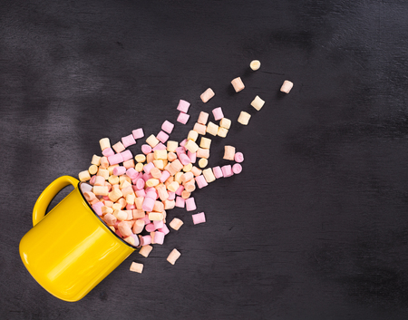 pieces of colored marshmallow scattered from a yellow mug, empty spaceの写真素材