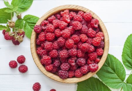 ripe red raspberries in a wooden bowl on a white table, top viewの写真素材