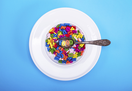 multicolored letters of the English alphabet in a white round plate with a spoon on a blue background, top viewの写真素材