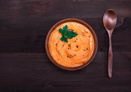 pumpkin soup in a round clay plate and a wooden spoon, top view