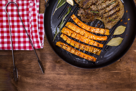 fried beef stack and fried carrots on a round frying pan, brown wooden background, top view, empty space at the bottomの写真素材