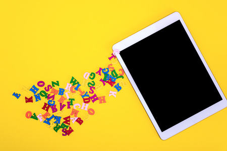 multicolored wooden letters and electronic tablet with a black screen on a yellow background