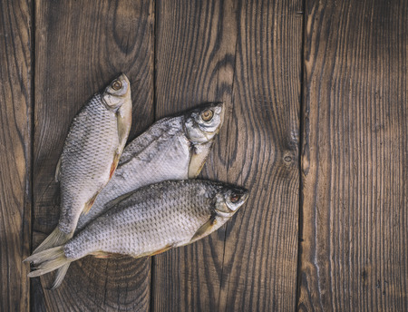 Three roach fish with scales on a brown wooden background, empty space on the right