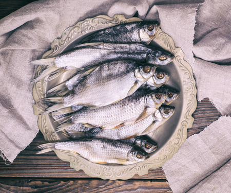 Dried salted fish ram in an iron plate on a brown wooden background, top viewの写真素材