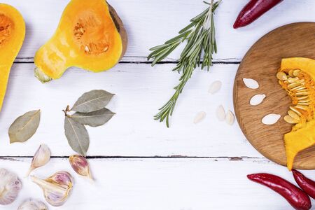 pieces of fresh pumpkin and spices on a white wooden background, empty space in the middleの写真素材