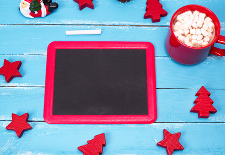 black chalkboard in a red frame on a blue wooden background and a red mug of hot chocolate with marshmallowsの写真素材