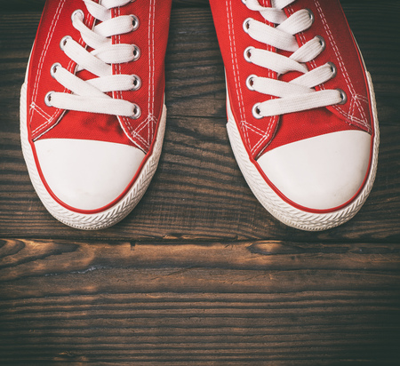 pair of red textile sneakers with white laces on a brown wooden background, top viewの写真素材
