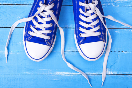 pair of blue textile shoes with loose white laces on a blue wooden background, top viewの写真素材