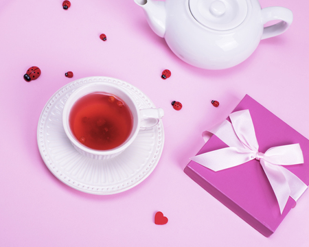 tea from berries of viburnum in a white ceramic mug and box with a gift on a pink backgroundの写真素材