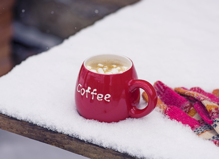 knitted mittens and a red cup with coffee on white snow, winter snowy dayの写真素材