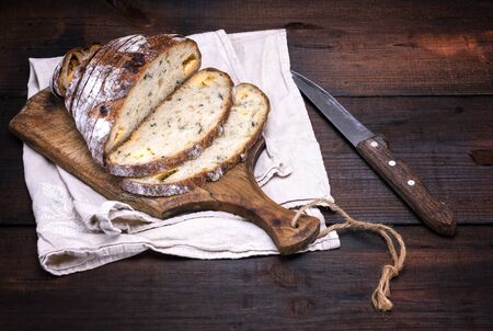 white bread from wheat with slices of cheese and spices is cut into slices on a brown wooden board