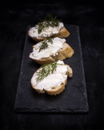 three sandwiches with white cream cheese on a slice of bread with dill, black background, top viewの写真素材