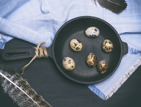 raw quail eggs in the shell lie in a black cast-iron frying pan, top viewの写真素材