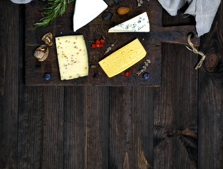 pieces of cheese on a brown cutting board: roquefort, brie, cheese with walnuts, top view, empty...