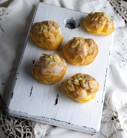 baked profiteroles with custard sprinkled with almonds on a white wooden board, top view