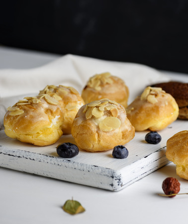 baked profiteroles with custard are sprinkled with almonds on a white wooden board, empty space at...