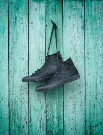 pair of black textile sneakers hanging on a green wooden wall, vintage toningの写真素材