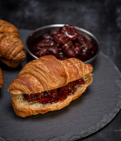 baked croissant with strawberry jam on a black background, close upの写真素材