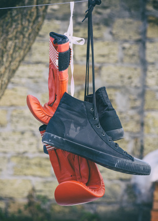 a pair of red boxing gloves and a pair of black textile sneakers hanging on a rope