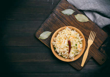 salad from sauerkraut, carrots and green onions in a brown wooden bowl on a kitchen cutting board, top view, empty space on the leftの写真素材