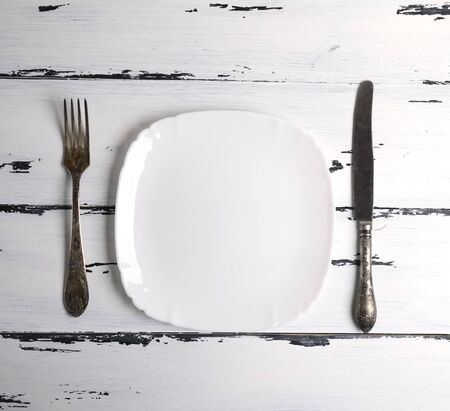 empty white ceramic plate with a fork and knife on a white wooden background, top viewの写真素材