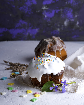 Easter baking with white sugar icing and colorful decor balls on a white table, empty space at the...