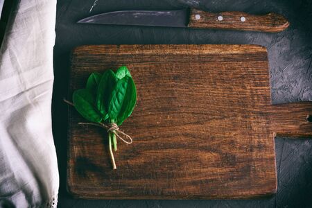 old brown wooden cutting board with handle and bunch with green sorrel leaves, top view, vintage...