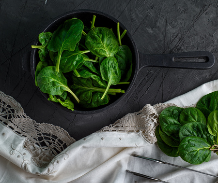 resh green spinach in a round cast-iron frying pan on a black background, top viewの写真素材