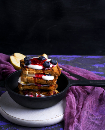 French toast with berries, syrup and sour cream in a black cast-iron frying pan, empty spaceの写真素材