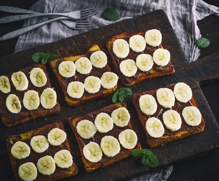 French toasts with chocolate and banana slices on a brown wooden cutting board, top viewの写真素材