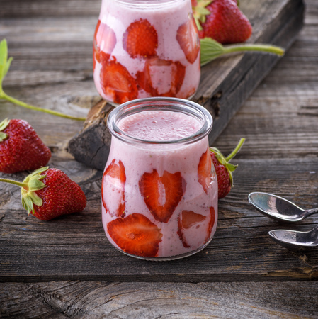 smoothies of fresh strawberries and yogurt in a glass jar on a gray wooden boardの写真素材