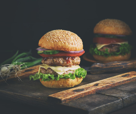 double cheeseburger in a bun with sesame seeds, in the middle fresh vegetables and meat cutlets, vintage toningの写真素材
