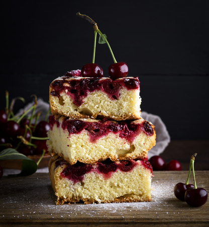 three slices in a pile of pies from a fresh cherry on a brown wooden board, black backgroundの写真素材