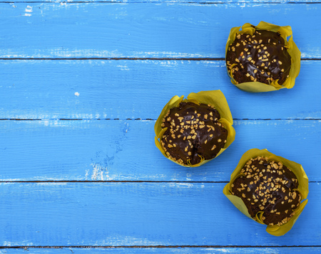 chocolate cupcakes wrapped in yellow paper on a blue wooden table, top view, copy spaceの写真素材
