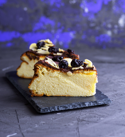 piece of cheesecake on a black background sprinkled with almond shavings and dry cherriesの写真素材