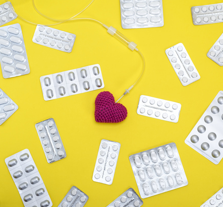 red heart and catheter on a yellow background in the middle of packages with white tablets, full...