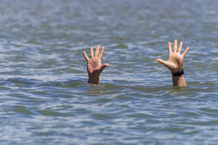 pair of masculine hands sticks out of the sea water on a summer day, a gesture of a man who sinks