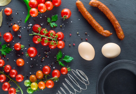two raw eggs in eggshell, fresh red cherry tomatoes and sausage, ingredients for cooking scrambled eggs, top view, black backgroundの写真素材