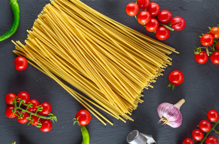 Uncooked pasta spaghetti on black background, red cherry tomatoes and garlic for sauce, top viewの写真素材