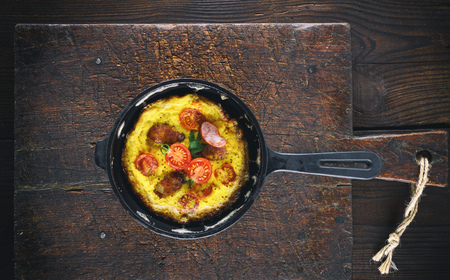 fried chicken eggs in a round black cast-iron frying pan on a brown old wooden cutting board, top viewの写真素材