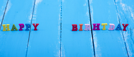 inscription made of wooden letters happy birthday on a blue wooden backgroundの写真素材
