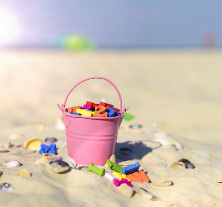 pink baby iron bucket filled with wooden colorful letters stands on the sand, close upの写真素材