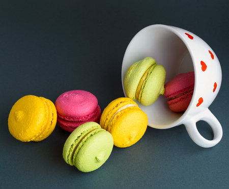 multicolored baked cakes of almond flour macarons in a white ceramic cup on a black backgroundの写真素材