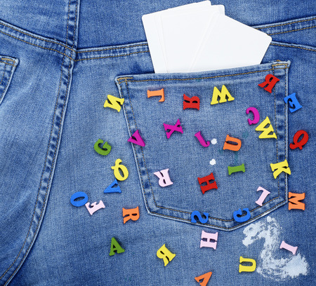 colored wooden letters scattered on blue jeans, inside the back pocket an empty white card, full frameの写真素材