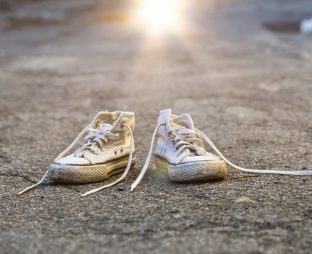 pair of very old white sneakers with untied laces on the pavementの写真素材